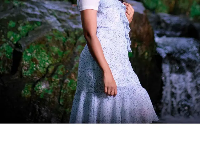 Pre-wedding portrait of a woman in a powder-blue gown beside mossy rocks and water