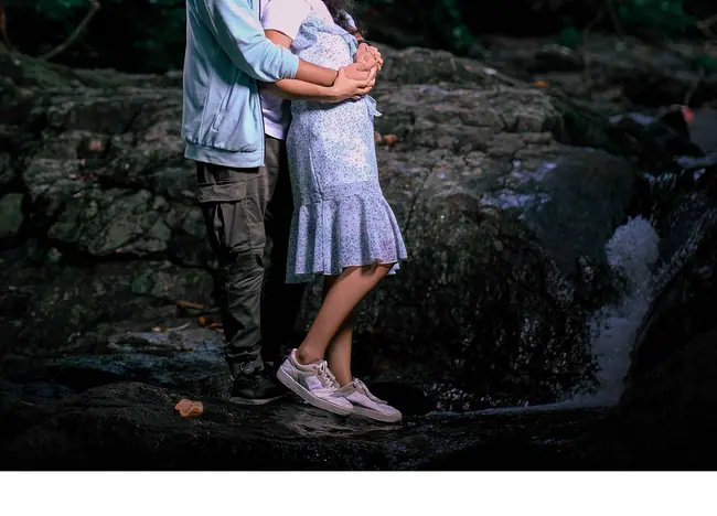Pre-wedding couple embracing on rocks beside a forest waterfall