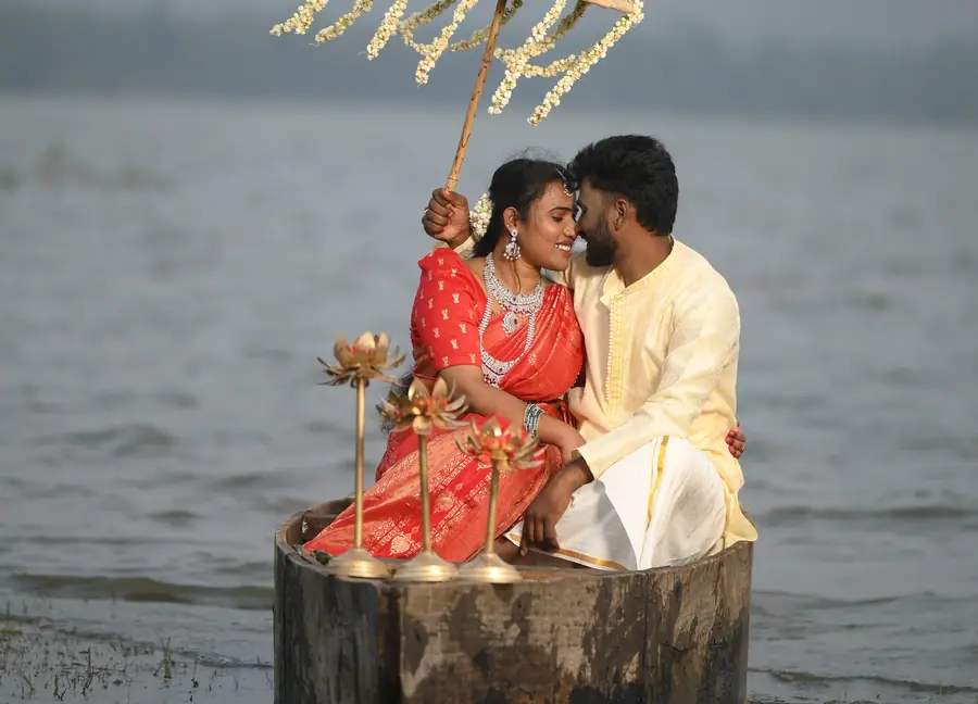 Pre-wedding couple seated on a lakeside set with a floral umbrella