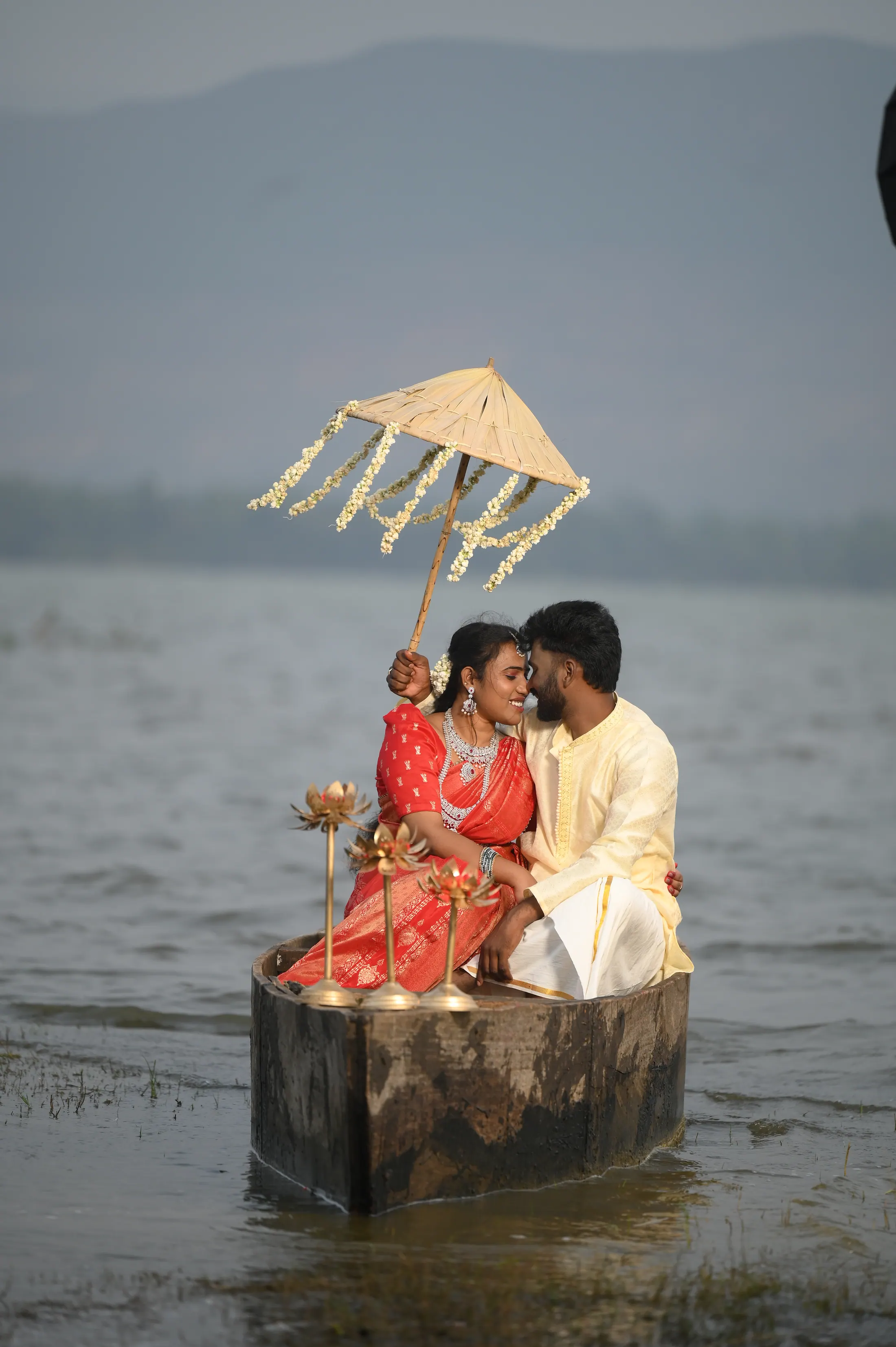 Pre-wedding couple seated on a lakeside set with a floral umbrella